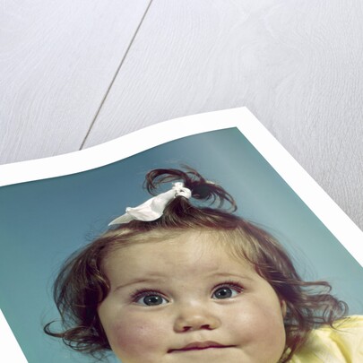 1960s brunette baby girl round chubby face yellow dress ribbon topknot interested sincere facial expression looking at camera by Anonymous