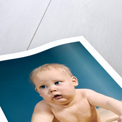 1960s baby big blue eyes raised up on arms looking to side by Anonymous