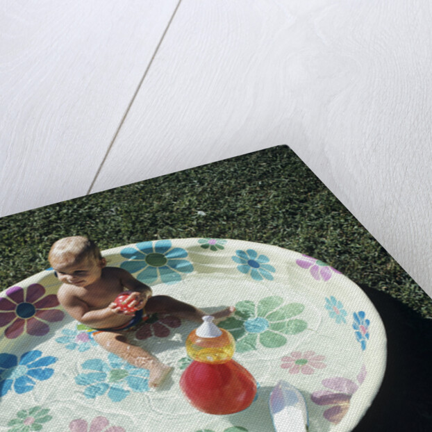 1970s baby sitting in plastic backyard kiddy pool viewed from above by Anonymous