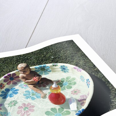 1970s baby sitting in plastic backyard kiddy pool viewed from above by Anonymous