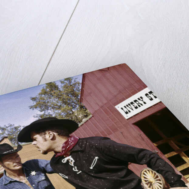 1960s cowboy sheriff with badge draws gun arrests gunfighter in front of livery stable by Anonymous