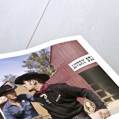 1960s cowboy sheriff with badge draws gun arrests gunfighter in front of livery stable by Anonymous