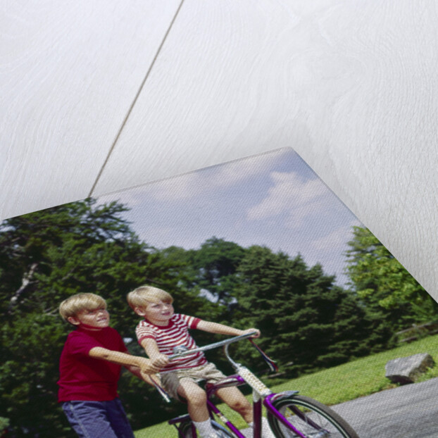 1960s 1970s boy helping little brother ride two wheel bicycle with training wheels by Anonymous