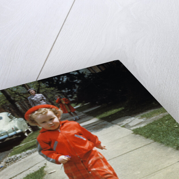 1950s little boy in red outfit running on pavement with mother just behind by Anonymous