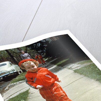 1950s little boy in red outfit running on pavement with mother just behind by Anonymous