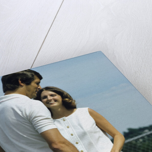 1970s smiling couple standing by net on tennis court holding wood rackets by Anonymous