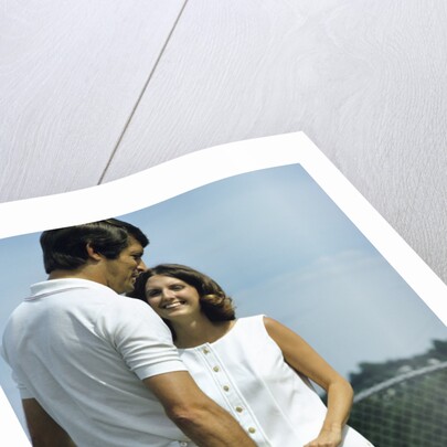 1970s smiling couple standing by net on tennis court holding wood rackets by Anonymous