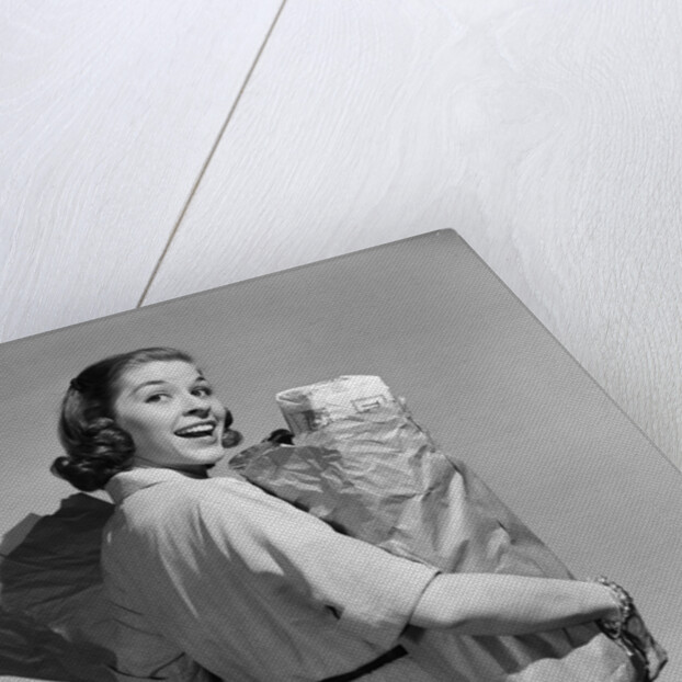1950s smiling woman carrying grocery bags both hands looking at camera over her shoulder by Anonymous