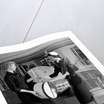 1950s woman in hat stole & gloves taking hatbox from saleswoman by Anonymous