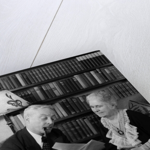 1930s 1940s retired senior couple looking at check in living room man smoking pipe by Anonymous