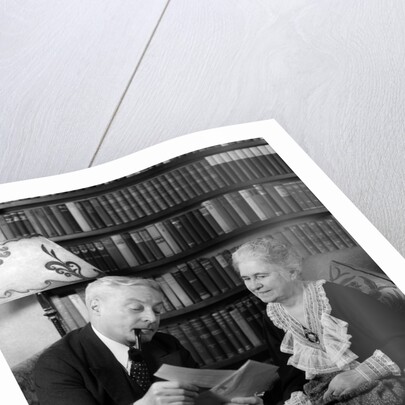 1930s 1940s retired senior couple looking at check in living room man smoking pipe by Anonymous