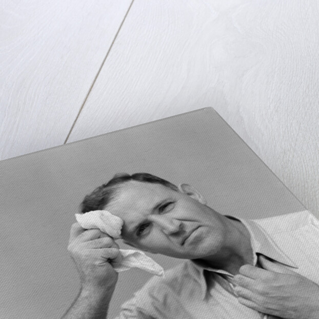 1940s 1950s perspiring man in rolled up shirt sleeves loosening tie holding handkerchief wiping forehead looking at camera by Anonymous