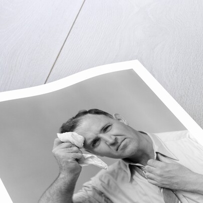 1940s 1950s perspiring man in rolled up shirt sleeves loosening tie holding handkerchief wiping forehead looking at camera by Anonymous