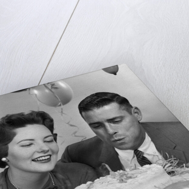 1950s 1960s couple with birthday anniversary cake man blowing out candle by Anonymous