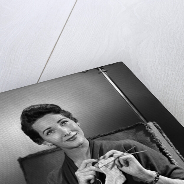 1950s woman crocheting baby sock looking at camera by Anonymous