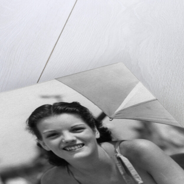 1930s teen girl lying on beach under umbrella wearing bathing suit smiling looking at camera by Anonymous