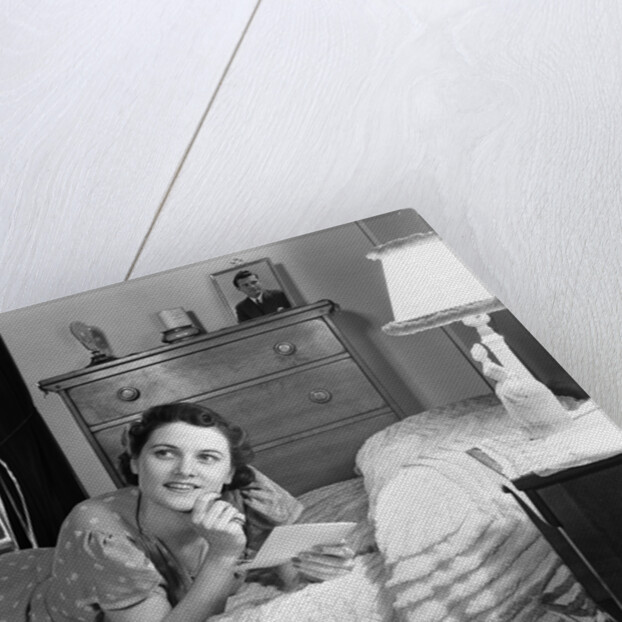 1940s fully dressed smiling woman laying on her bed with her legs up reading a letter in her bedroom by Anonymous