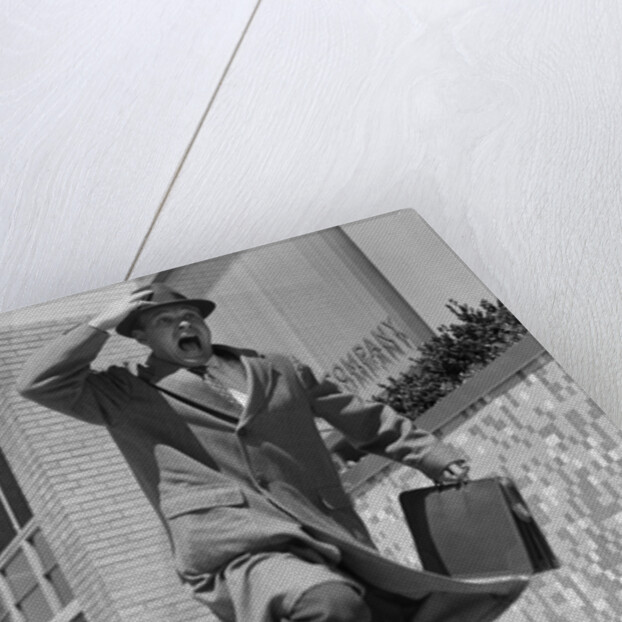 1960s 1950s frantic man running down street holding hat on with hand carrying briefcase wearing top coat by Anonymous