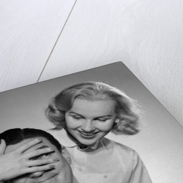 1950s woman standing behind man with hand over his eyes by Anonymous