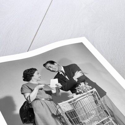 1950s couple man woman shopping cart reviewing grocery list man has cigar in hand by Anonymous