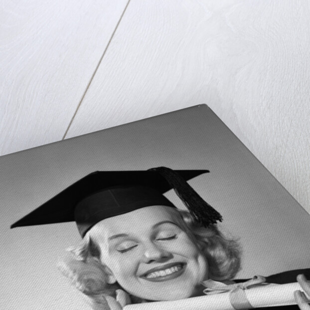 1950s smiling woman teenage girl eyes closed holding diploma graduate wearing cap gown by Anonymous