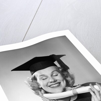 1950s smiling woman teenage girl eyes closed holding diploma graduate wearing cap gown by Anonymous