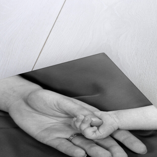 1950s close-up of baby holding mother's thumb by Anonymous