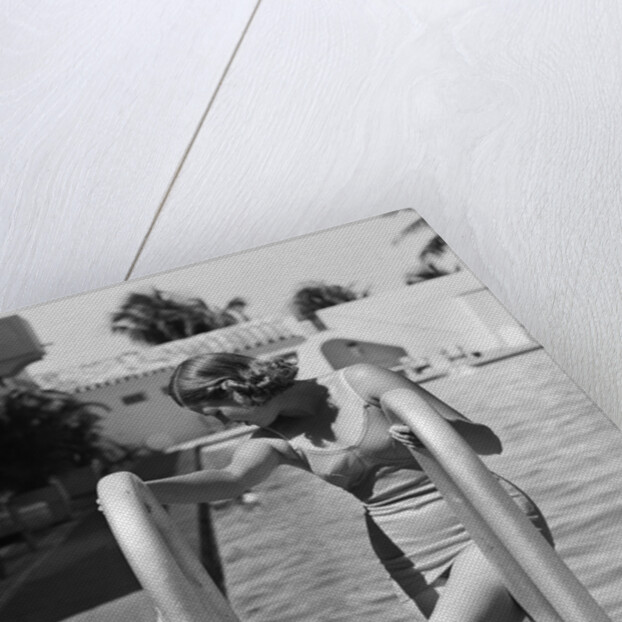 1930s woman wearing one piece bathing suit climbing out of swimming pool looking down at man smiling by Anonymous