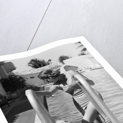 1930s woman wearing one piece bathing suit climbing out of swimming pool looking down at man smiling by Anonymous