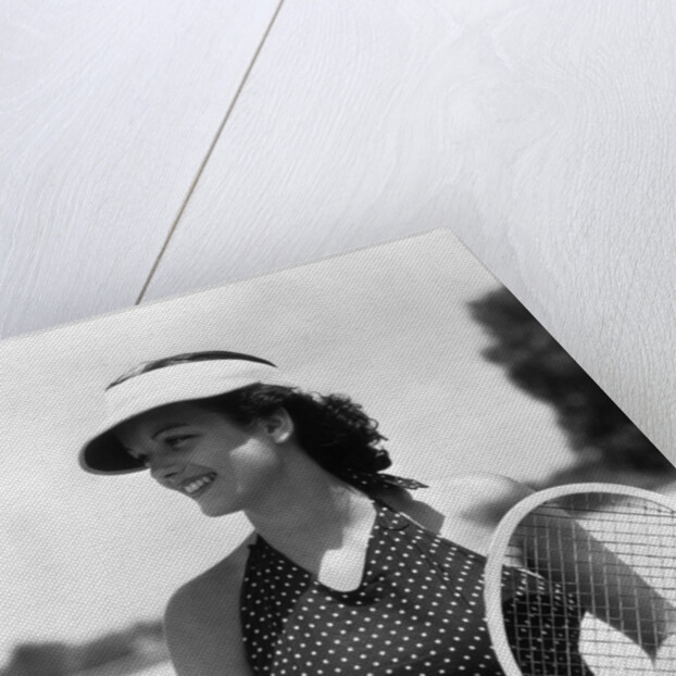 1930s woman in polka dot halter top shorts & sun visor holding a tennis ball & racket by Anonymous