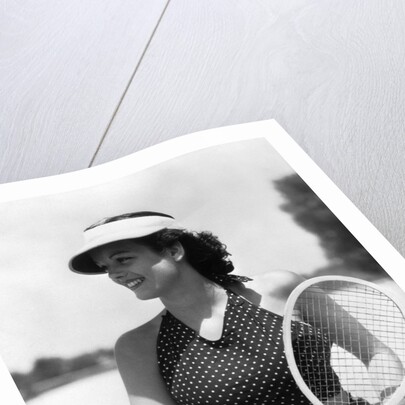 1930s woman in polka dot halter top shorts & sun visor holding a tennis ball & racket by Anonymous