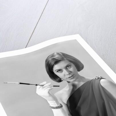 1960s formally elegantly dressed young woman looking at camera with a cigarette holder wearing long white gloves by Anonymous