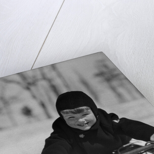 1930s young smiling boy on sled in snow looking at camera by Anonymous