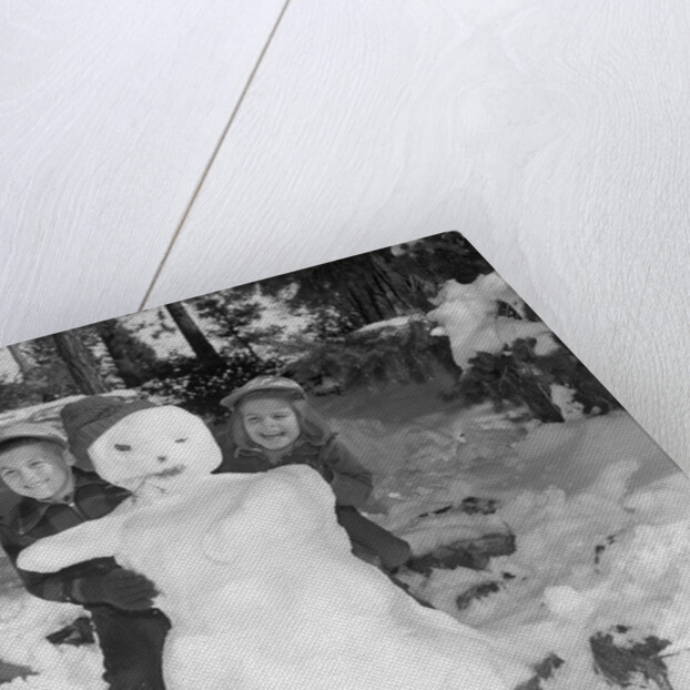 1950s 1960s smiling boy and girl building a snowman together in snowy woods by Anonymous