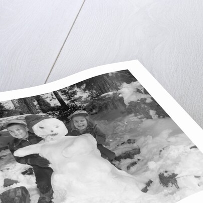 1950s 1960s smiling boy and girl building a snowman together in snowy woods by Anonymous