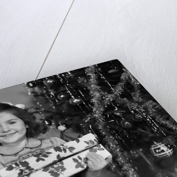 1940s little girl standing near christmas tree holding a wrapped present smiling looking at camera by Anonymous