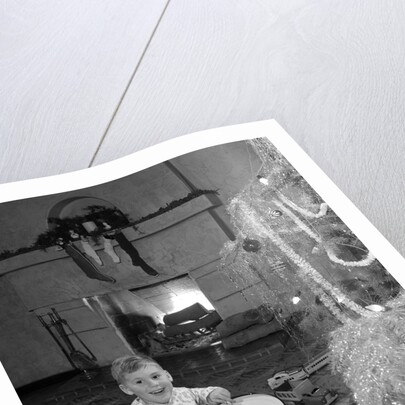 1950s little boy playing toy drum by christmas tree and fireplace looking at camera by Anonymous