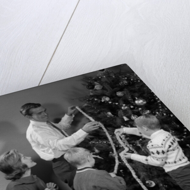 1960s family father mother two sons trimming christmas tree with string of popcorn by Anonymous