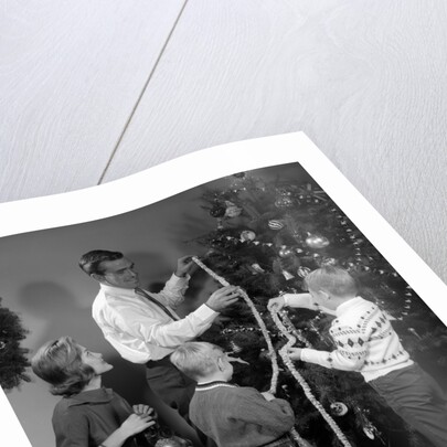 1960s family father mother two sons trimming christmas tree with string of popcorn by Anonymous