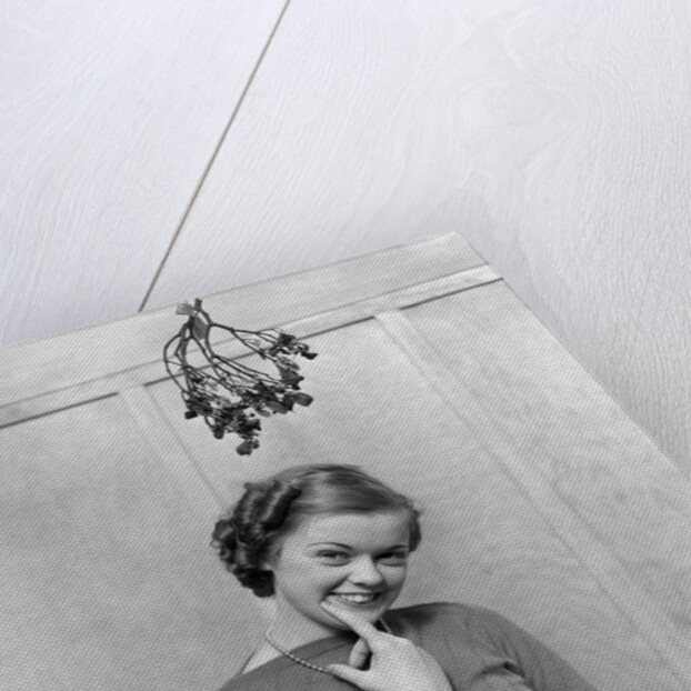 1930s 1940s cute young woman standing under mistletoe smiling hand near mouth looking at camera by Anonymous