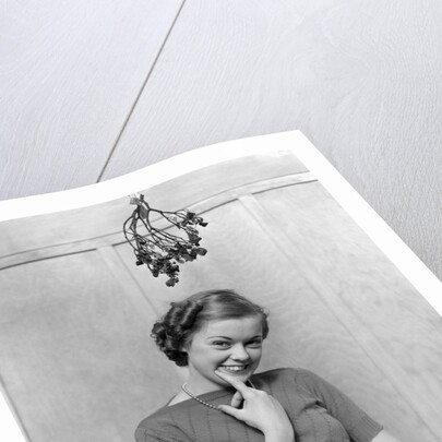 1930s 1940s cute young woman standing under mistletoe smiling hand near mouth looking at camera by Anonymous