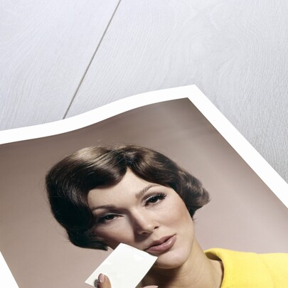1960s Brunette Woman Holding Blank Business Card To Face Looking At Camera Wearing Yellow Top by Anonymous