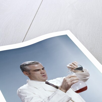 1960s Man Wearing Lab Coat Pouring Liquid From Small Erlenmeyer Flask Into A Larger Flask by Anonymous
