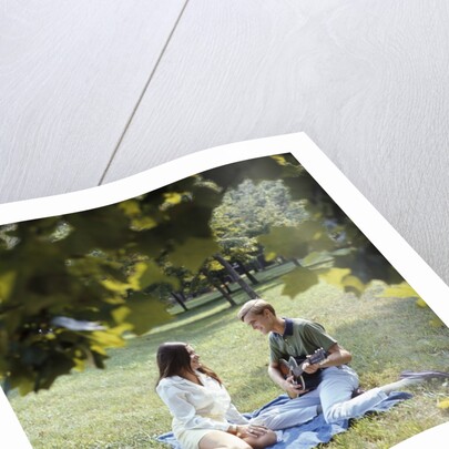 1960 1960s 1970 1970s Retro Smiling Couple Man Woman Sitting On Blanket On Grass Park Man Playing Acoustic Guitar by Anonymous