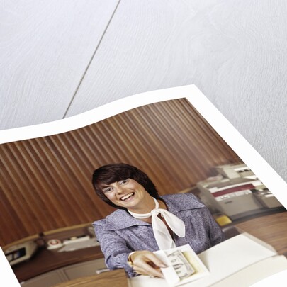 1970s Smiling Woman Bank Teller Handing Cash Over Counter by Anonymous