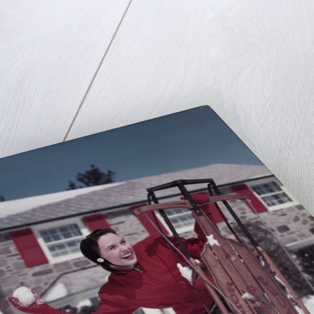 1950s Woman Hiding Behind Sled Throwing Snowball Front Stone House by Anonymous
