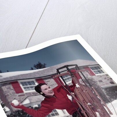 1950s Woman Hiding Behind Sled Throwing Snowball Front Stone House by Anonymous