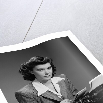 1940s Serious Secretary Stenographer Woman With Pencil Checking Notepad Sitting At Desk With Manual Typewriter Looking At Camera by Anonymous