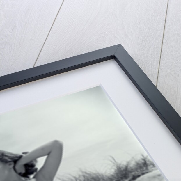 1950s Brunette Bathing Beauty In Polka Dot Bikini Standing In Sand With Hands Behind Head Looking At Camera by Anonymous