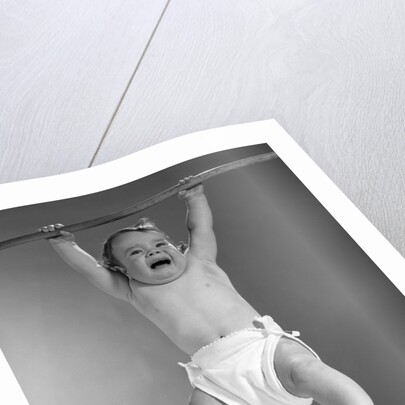 1960s Baby Hanging From Rod With Frightened Expression On Verge Of Tears by Anonymous